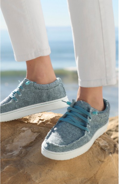 Image depicting a woman wearing casual shoes walking on the rocks with the ocean in the background.