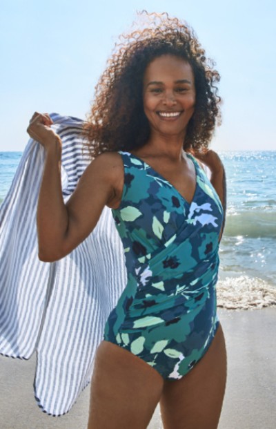 Woman wearing one-piece swim suit holding a beach towel. 