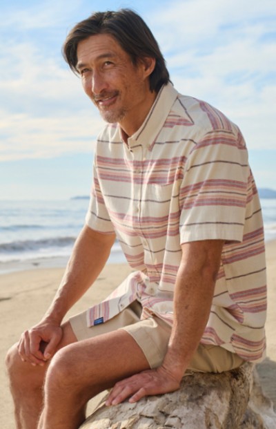 Image of a man sitting on a log at the beach with ocean in the background.