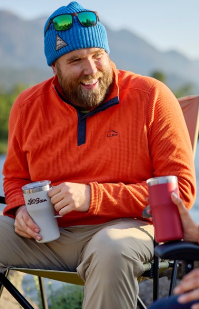 Image of a man sitting in a camp chair drinking coffee with mountains in the background.