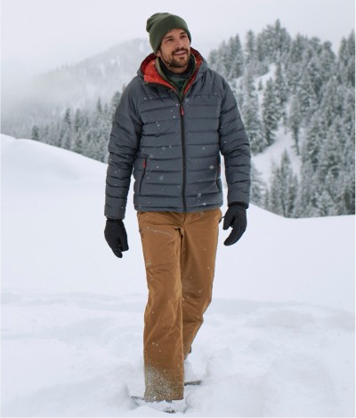 A man on snowshoes walking across a snowy field in the mountains.