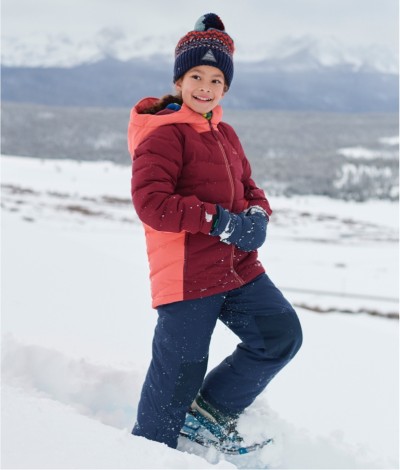 A smiling kid on snowshoes walking across a snowy field, snow-capped mountains in the distance.