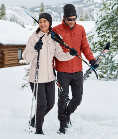 A couple carrying cross-country ski equipment walking through the snow.