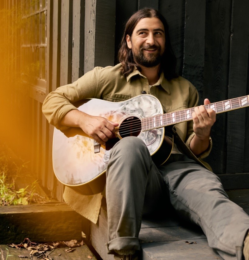 Noah Kahan playing a guitar outside.