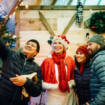 4 people outside, one in a Mrs. Claus costume, posing for a selfie.