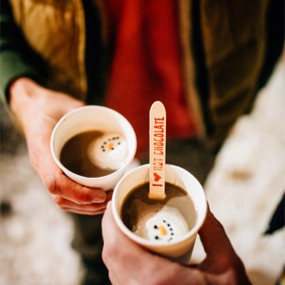 A close-up of 2 mugs of hot cocoa and the hands that hold them.