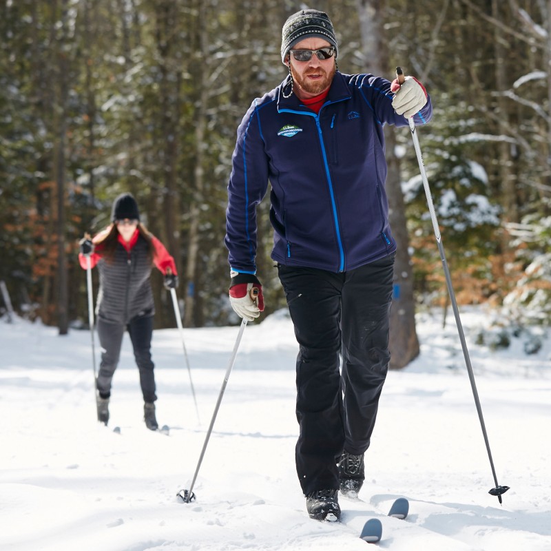 A male and female partake in cross country skiiing.