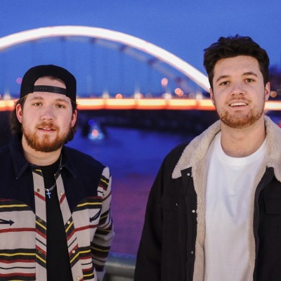 The 2 men of 12OC band, a lit bridge in the background.