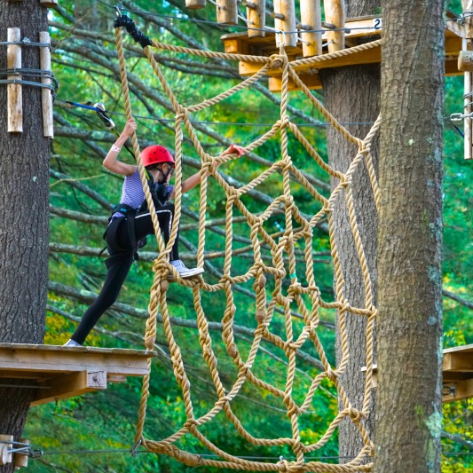 A young person climbing on a rope spider web.