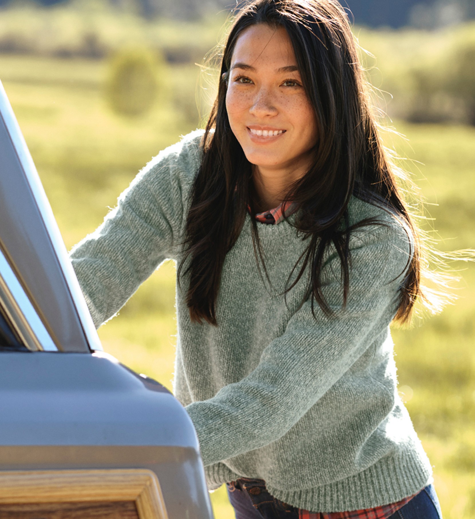 A woman outside reaching into the back of a car wearing a Ragg Wool Sweater.