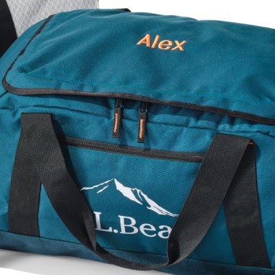 A teal L L Bean duffel bag with the name Alex embroidered on it, resting on a surface, ready for an adventure.