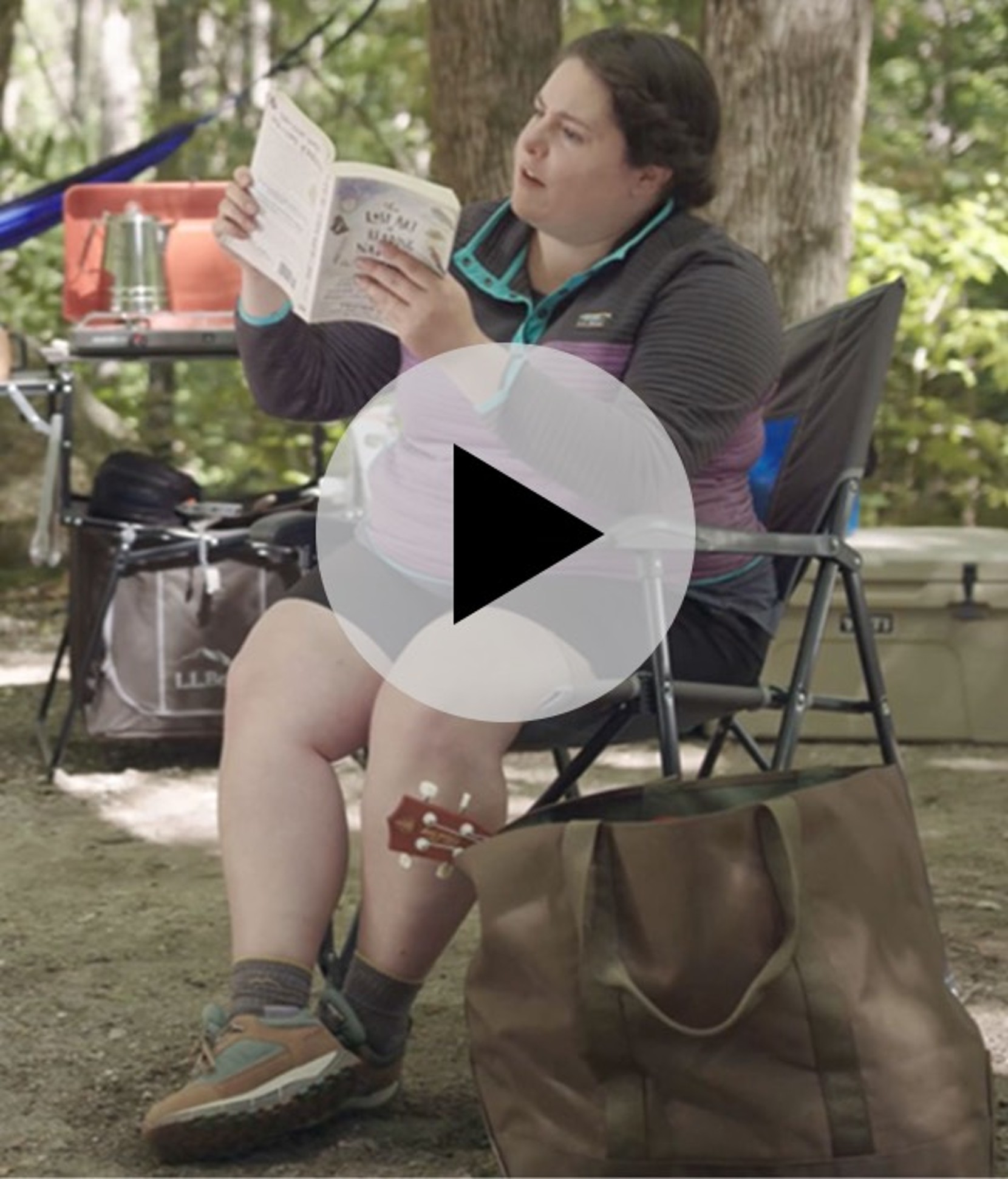 A woman sitting in a chair reading a book at a campsite