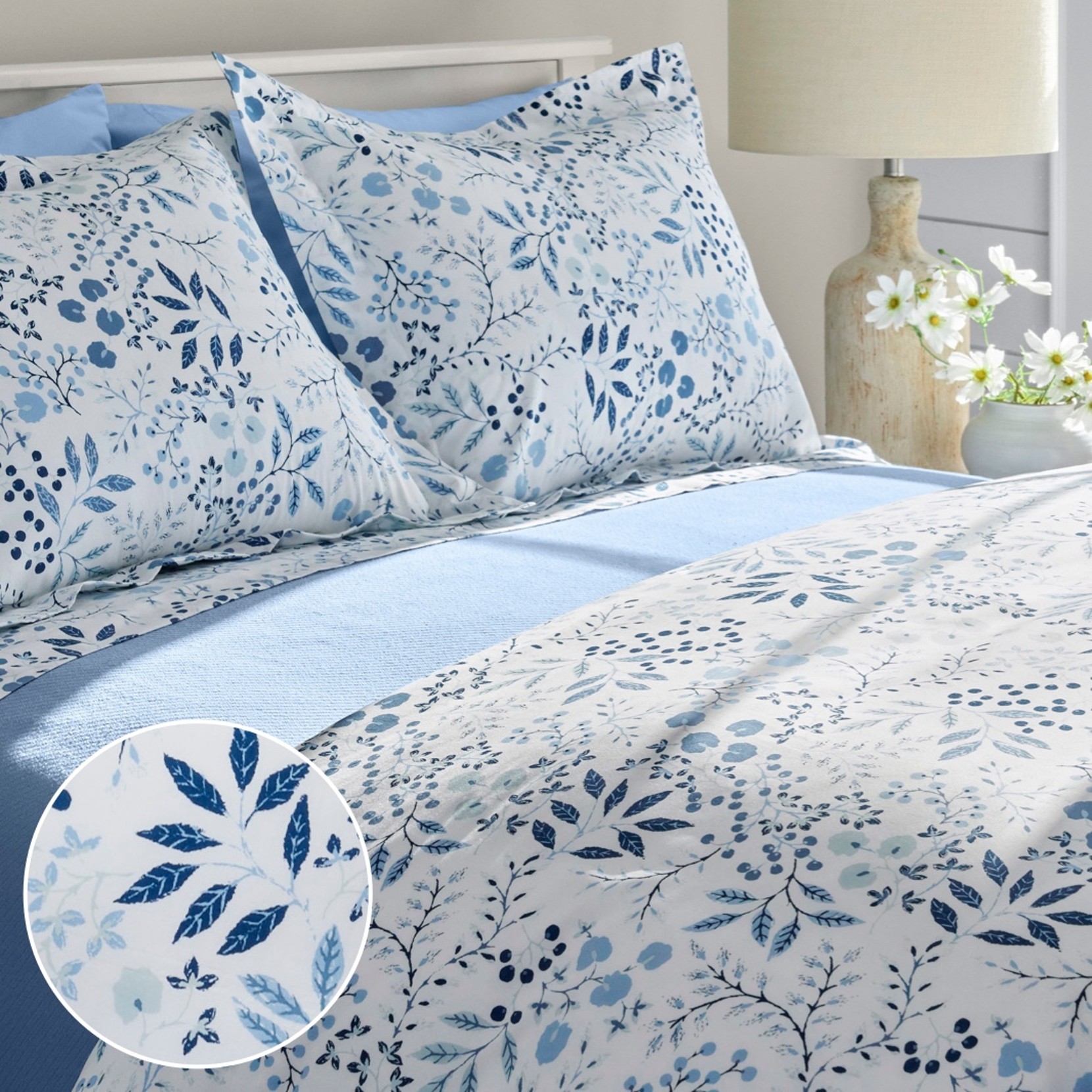 Floral bedding set with blue botanical print, matching pillow shams, and light blue sheet in a bright bedroom setting.