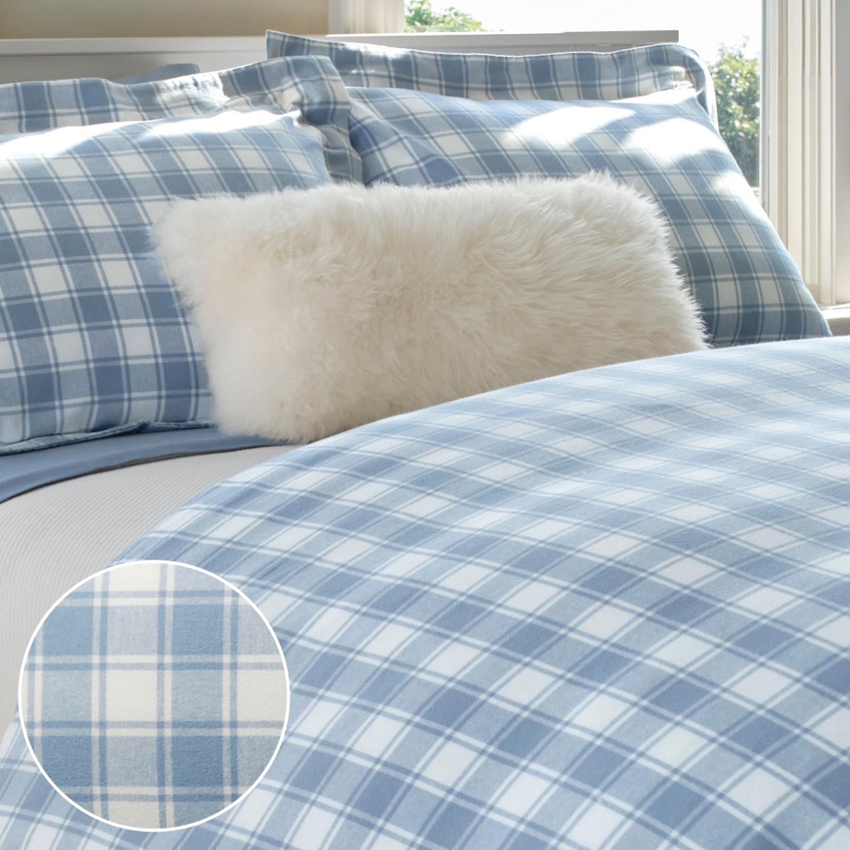 Flannel bedding set with blue plaid print, matching pillow shams, and light blue sheet in a bright bedroom setting.