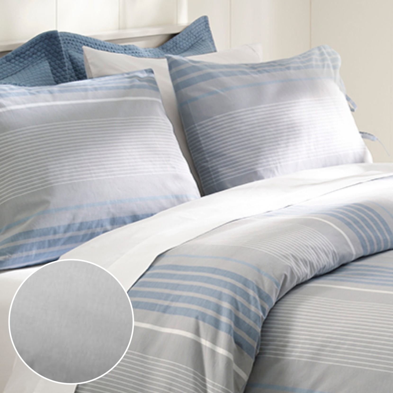 Striped bedding set with blue striped print, matching pillow shams, and light blue sheet in a bright bedroom setting.
