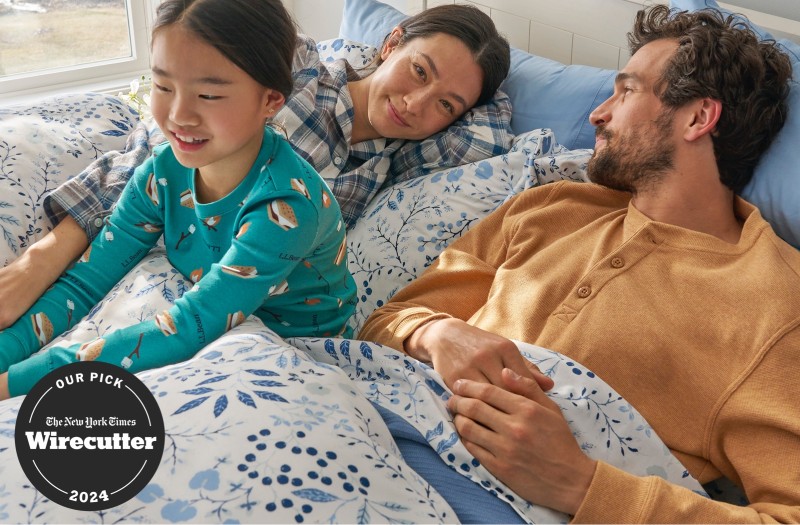 Parents and child in pajamas while lounging on a cozy bed with blue floral print