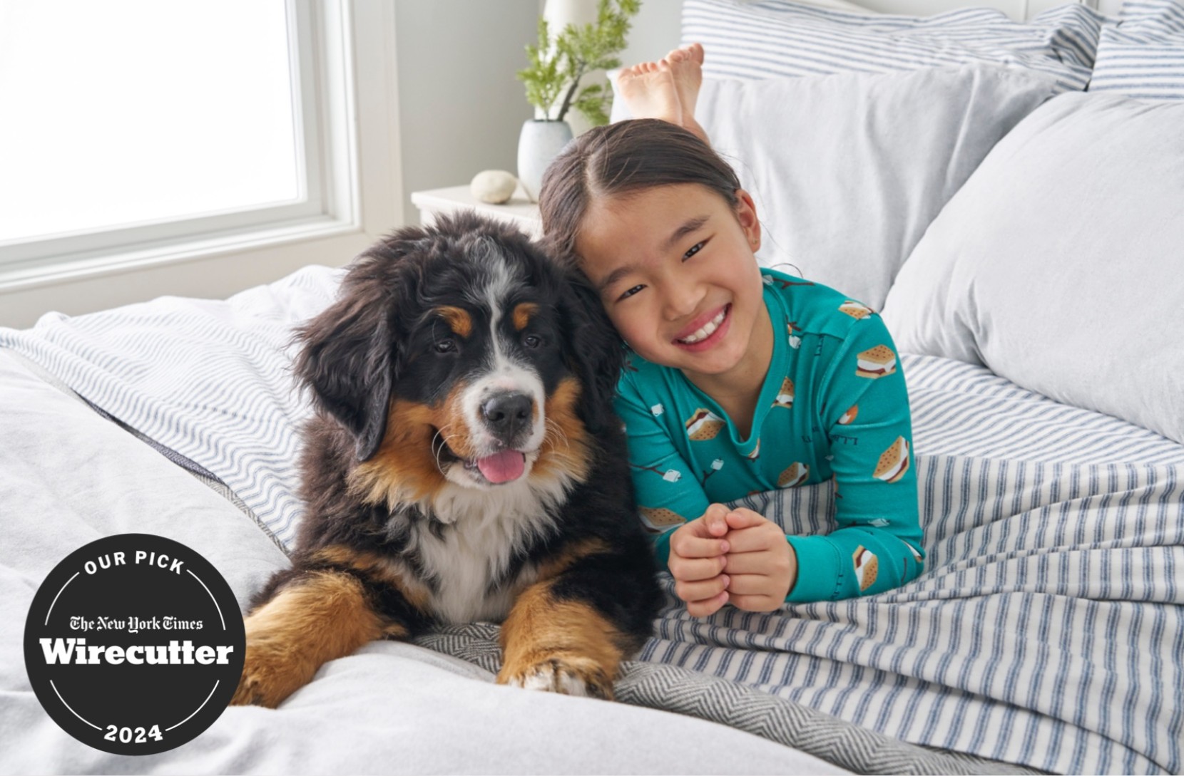 Child in teal pajamas lying on striped bedding beside a Bernese mountain dog; Wirecutter 2024 Our Pick badge shown.