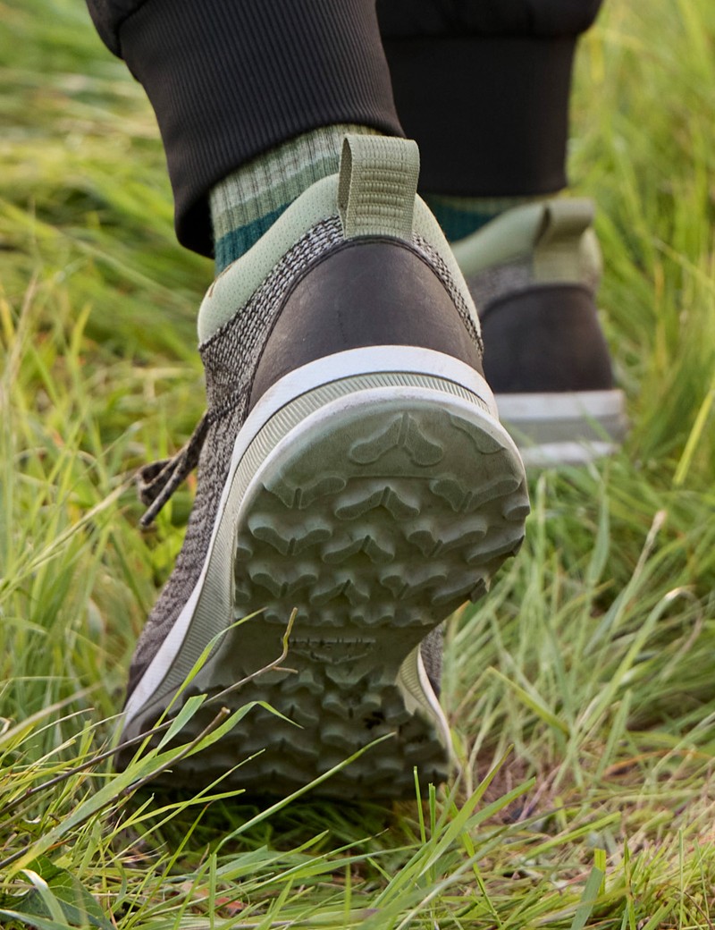 A person wearing green and brown sneakers running on grass.