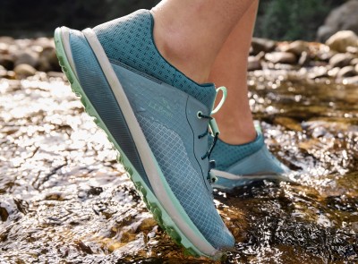 A close-up of hiking footwear on a person walking across rocks.