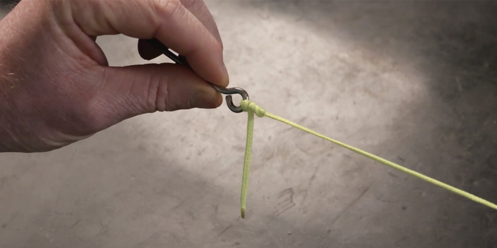 A hand holding a metal hook with a yellow string tied in a knot around it.