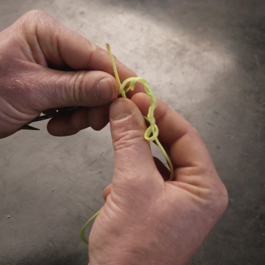 Hands pass the tag end through the loop forming at the eye of a fishing hook.