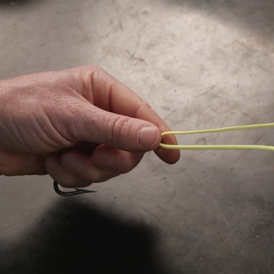 9 inches of fishing line is threaded through the fishing hook eye, as hands pinch the tag and standing line together.