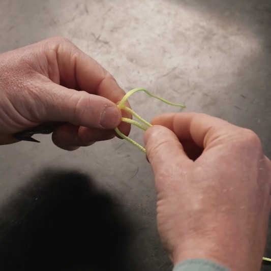 Hands form a loop with the tag end over the standing line, while fingers pinch them together.