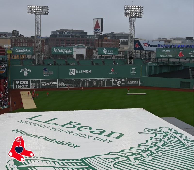Fenway Park field covered with a tarp featuring L.L. Bean logo and #BeanOutsider, with the Green Monster in the background.