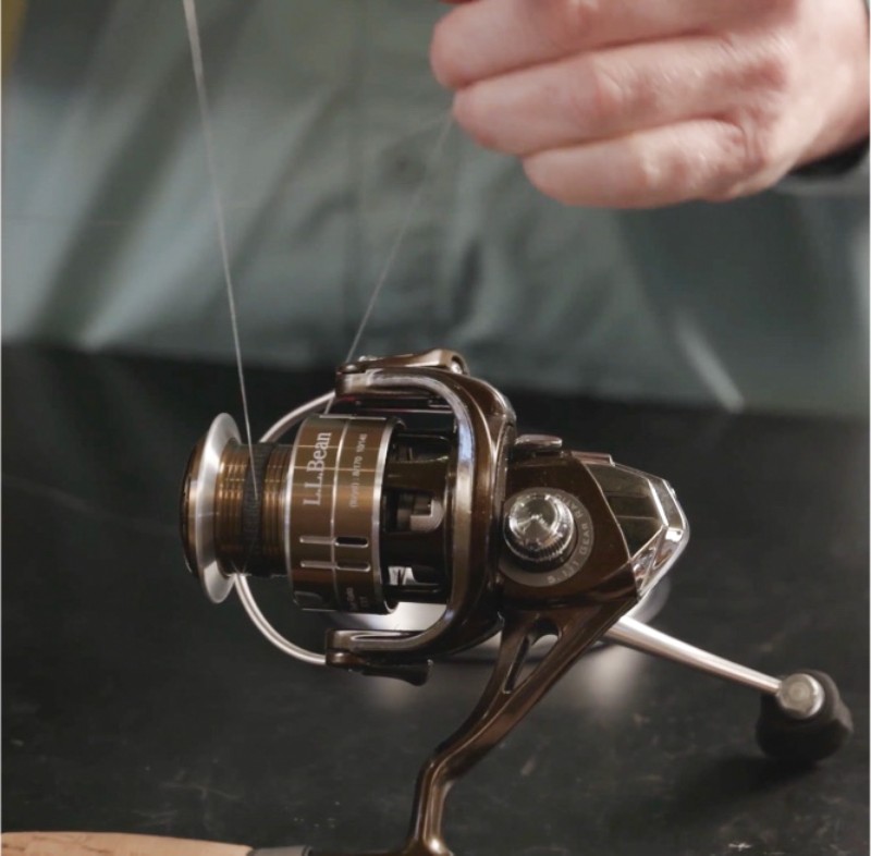 A person is threading a fishing line onto an L L Bean fishing reel. 