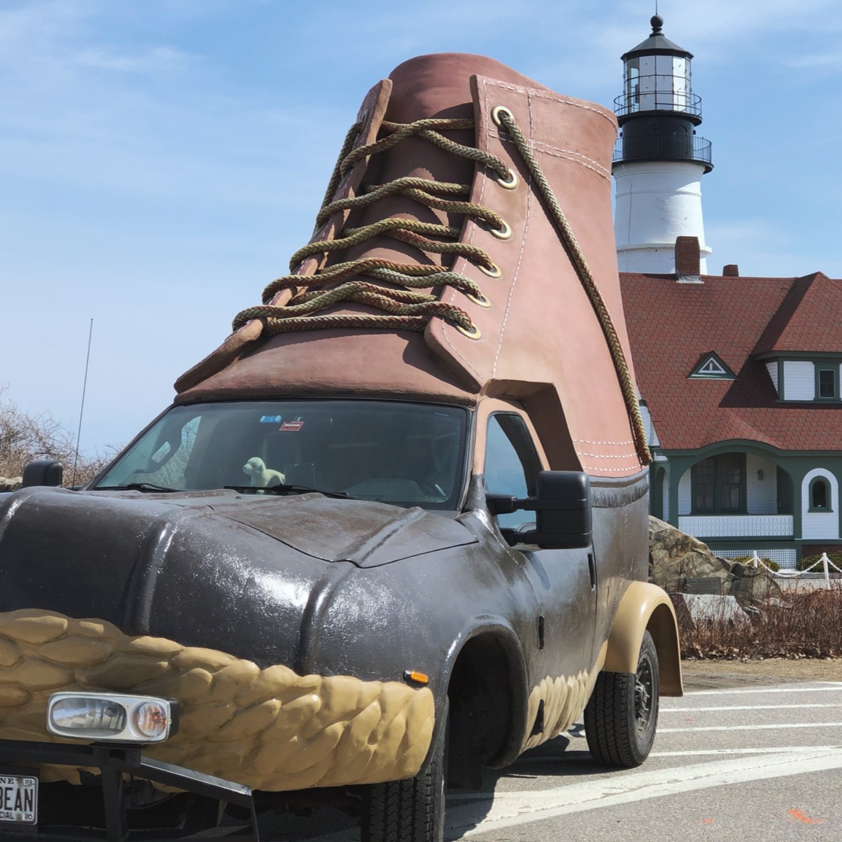 A truck designed to look like a giant L L Bean Boot is parked in front of the Portland Head Light lighthouse.