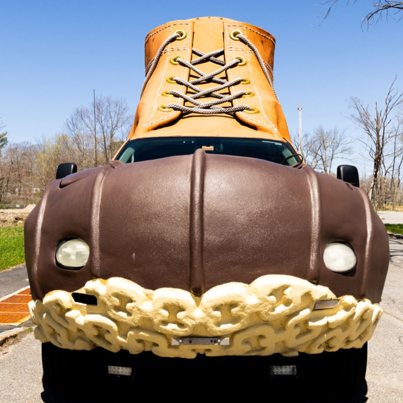 A truck designed to look like a giant L L Bean Boot, parked on a road with trees in the background.