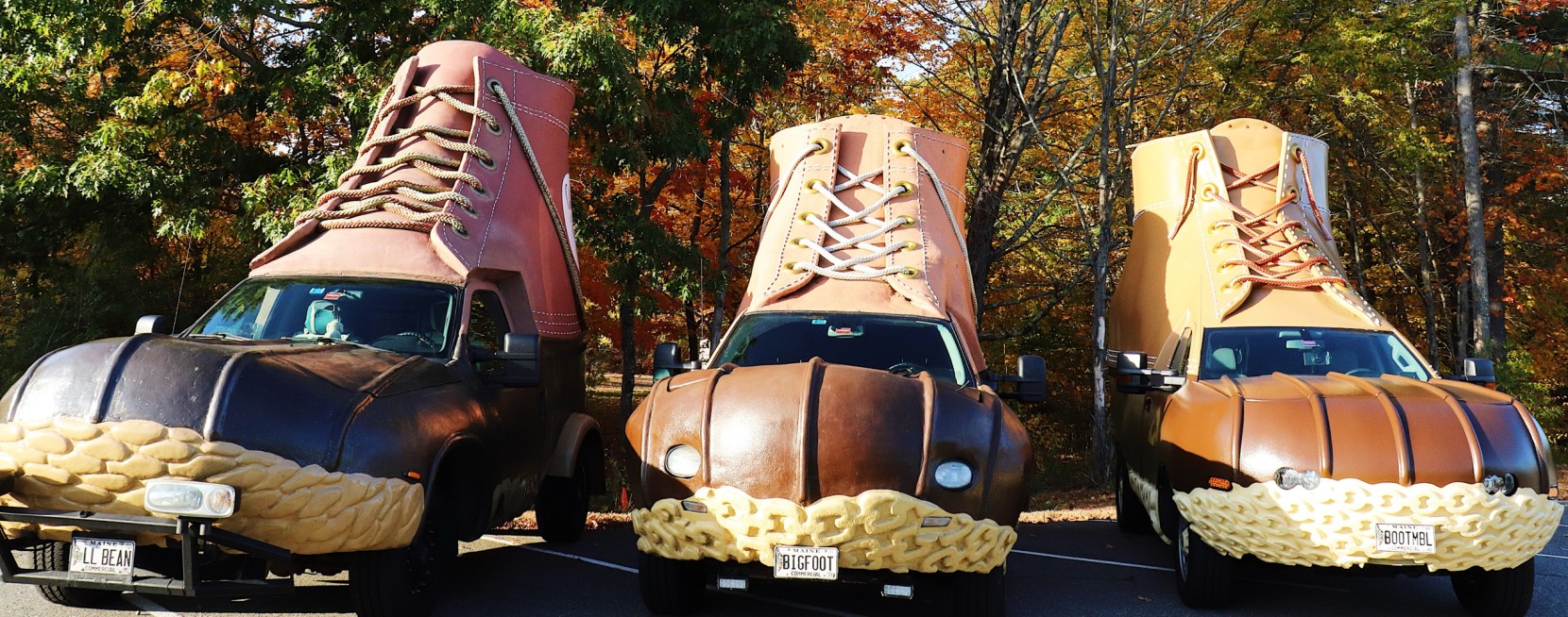 Three cars designed to look like giant brown leather boots with laces are parked side by side in a wooded area.
