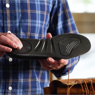 A person in a blue plaid shirt holds up the black rubber sole of a shoe, showing its tread pattern. 