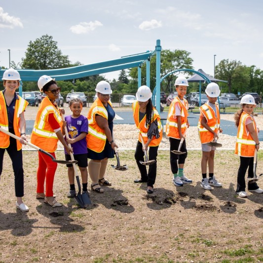 Kids in hard hats and orange vests breaking ground at a Trust for Public Land ceremony.