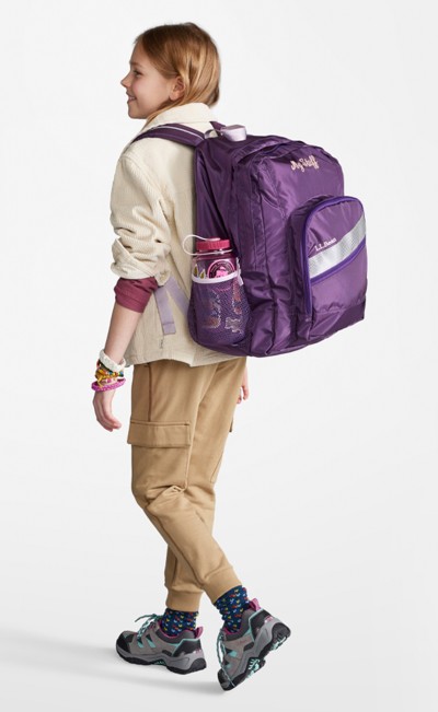 A girl from slightly behind, wearing a purple deluxe school backpack.