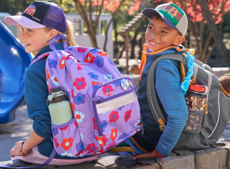 Close-up of 2 kids back-to looking left wearing L. L. Bean school backpacks.