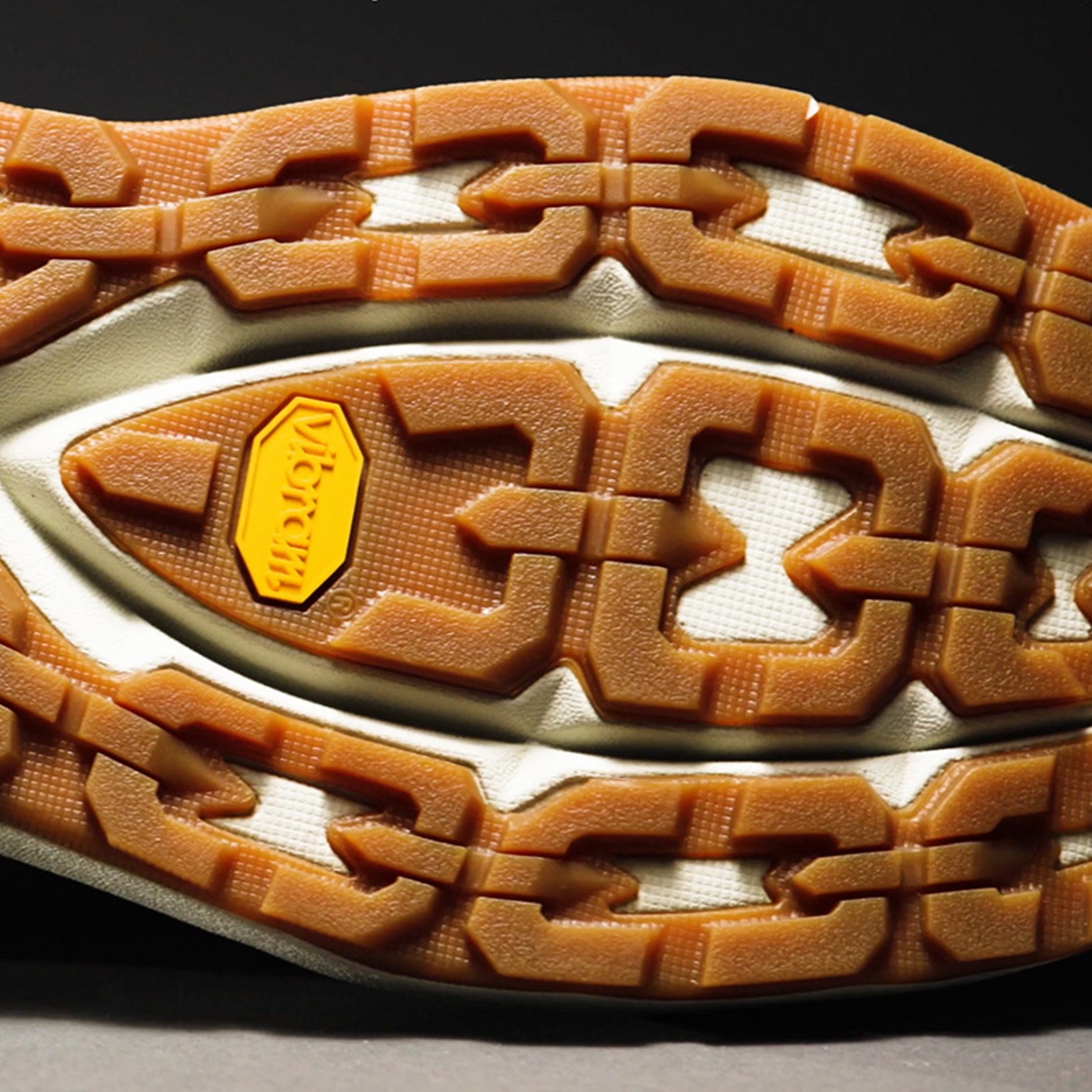 Close-up of shoe sole with unique tread pattern and orange Vibram logo in the center.