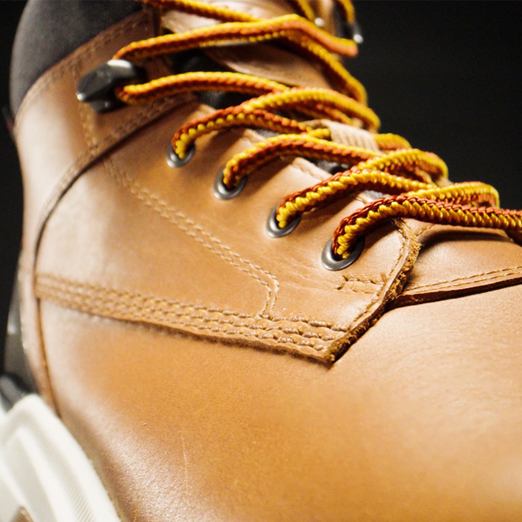 Close-up of brown leather shoe with yellow laces against a black background.