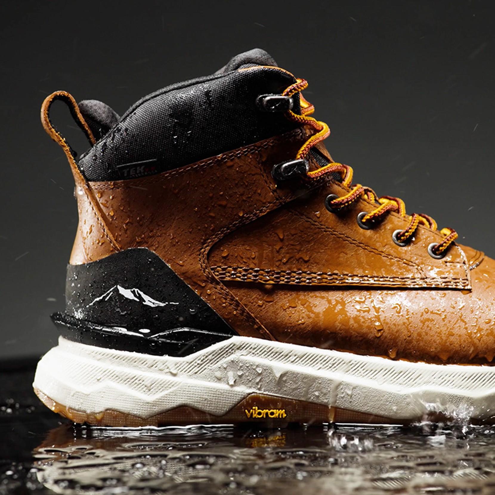 Brown waterproof hiking boot with black accents, yellow laces, white sole, water droplets, and visible Vibram logo.