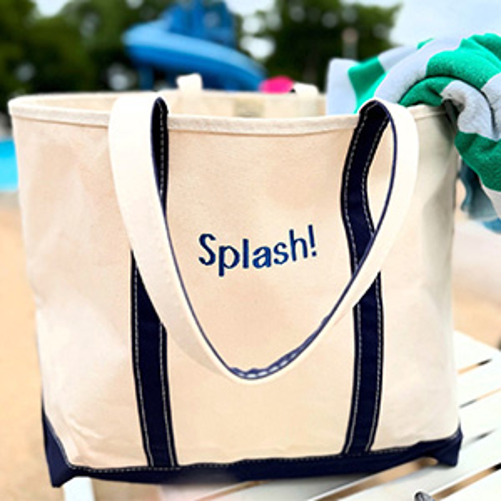 "Splash!" tote with blue straps by a pool, filled with towels.