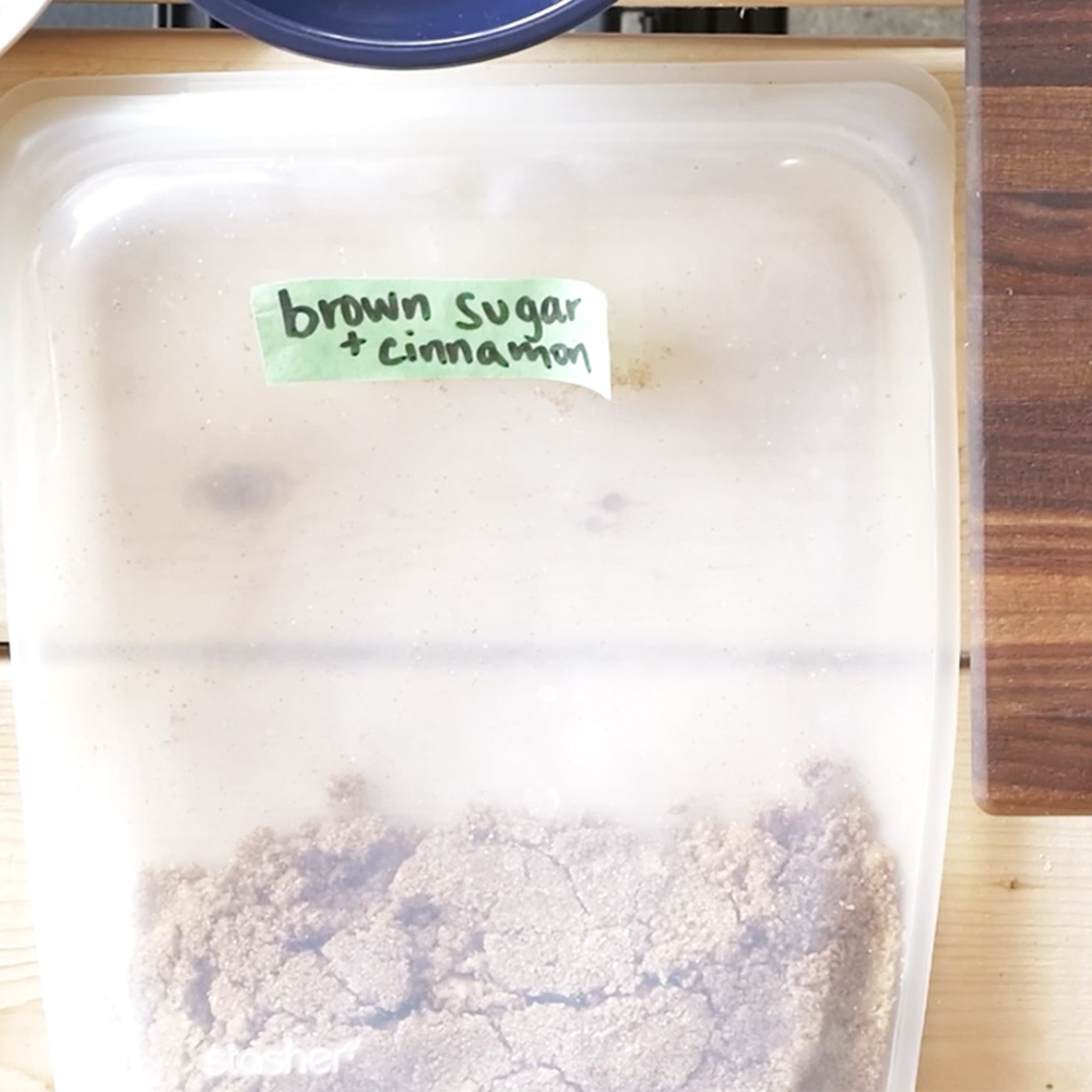 Plastic container labeled “brown sugar + cinnamon” with green tape, partially filled with brown sugar and cinnamon mixture.
