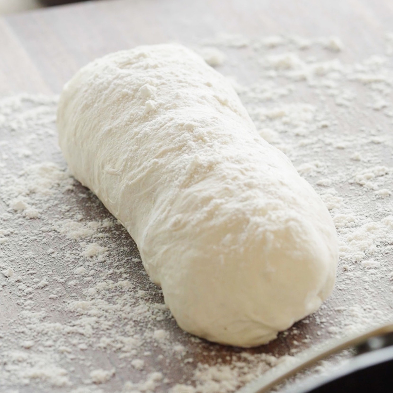 Ball of raw dough coated in flour on a floured wooden surface. 