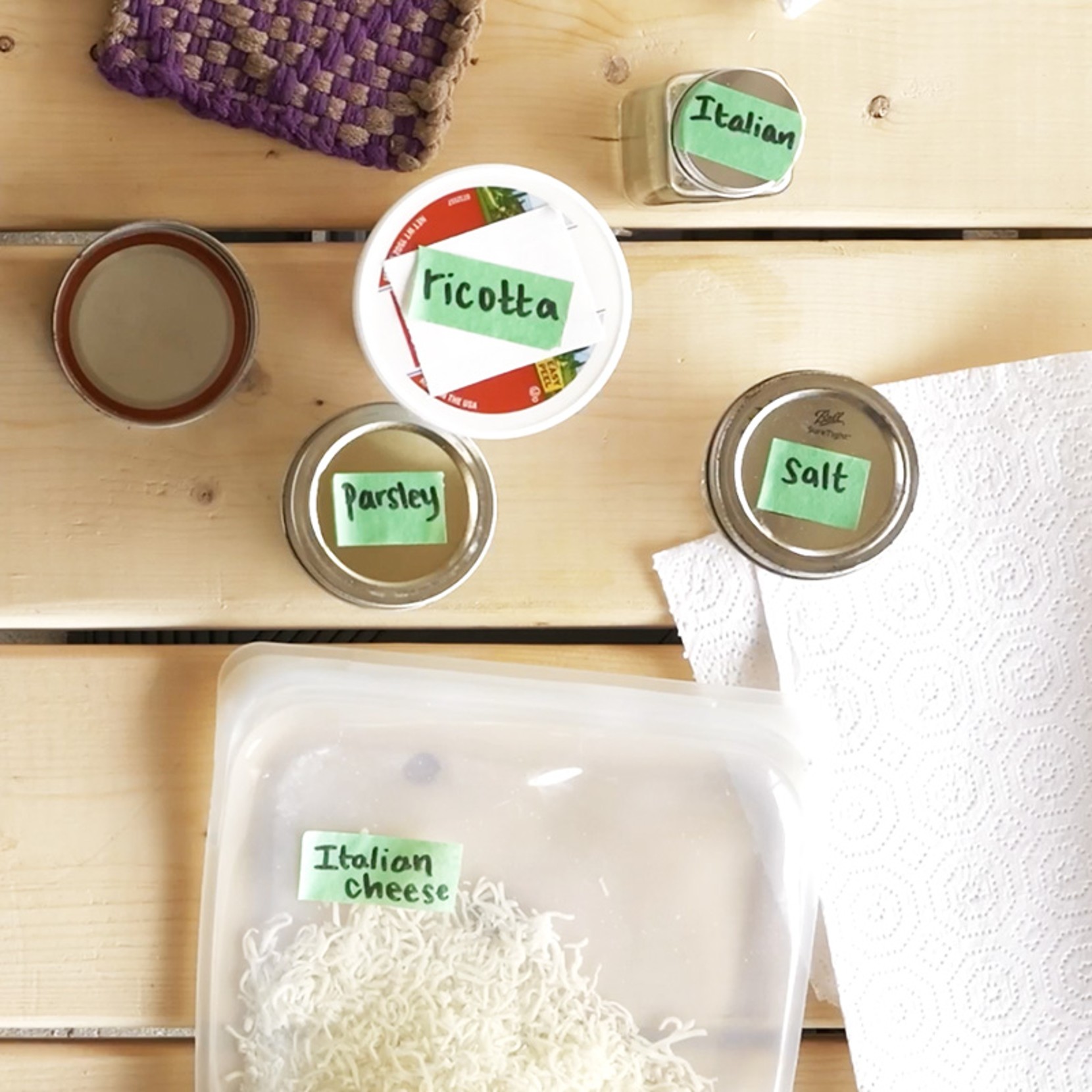 Labeled jars and containers of ricotta, parsley, salt, Italian seasoning, and cheese on a wooden surface.
