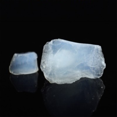 Two translucent blue aerogel pieces, one large and one small, rest on a reflective black surface.