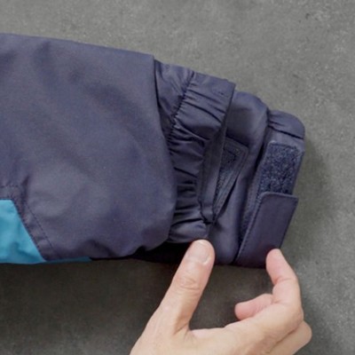 Hands adjust the sleeve of a blue and navy winter jacket on a gray surface.