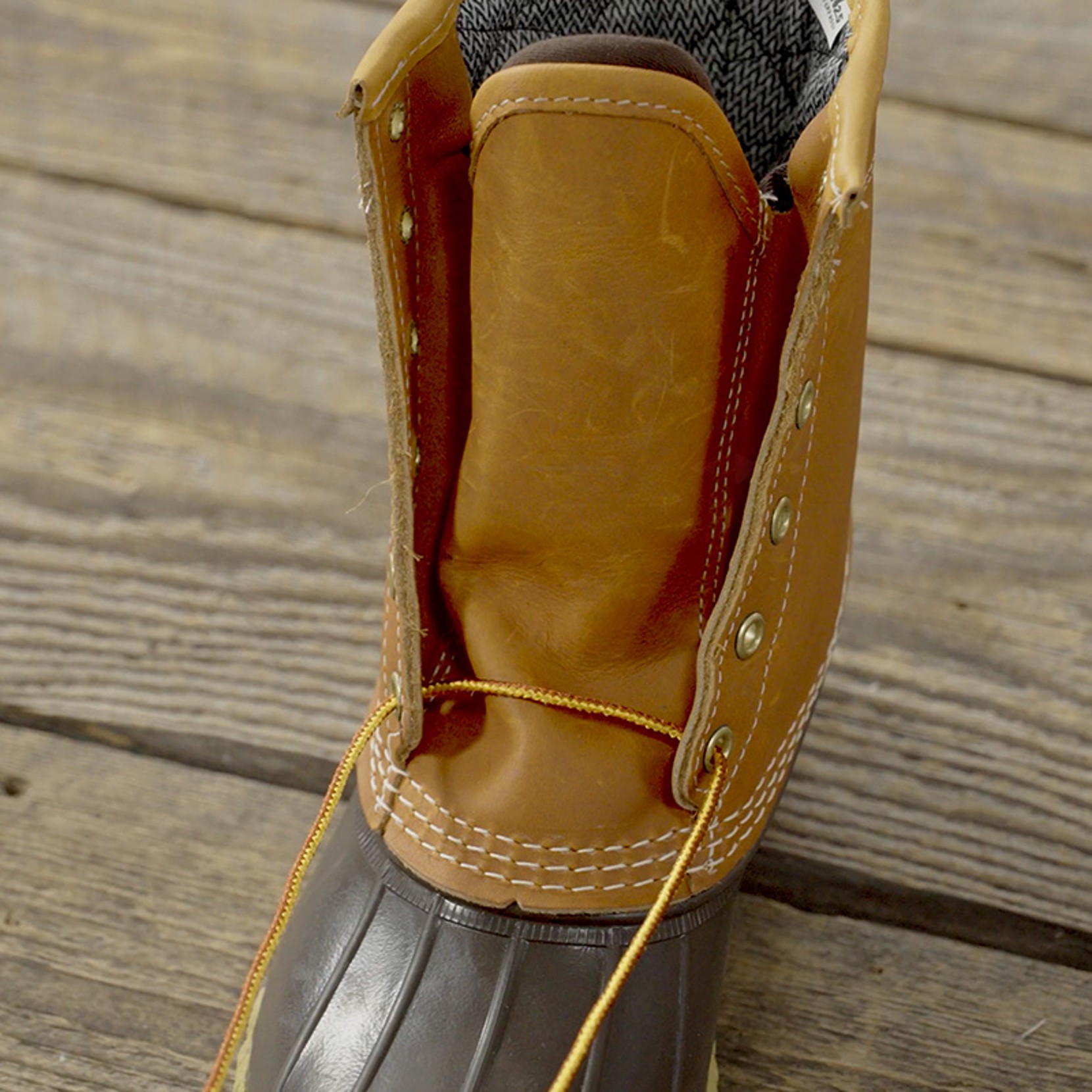 Close-up of an open brown leather boot with yellow laces on a wooden floor.