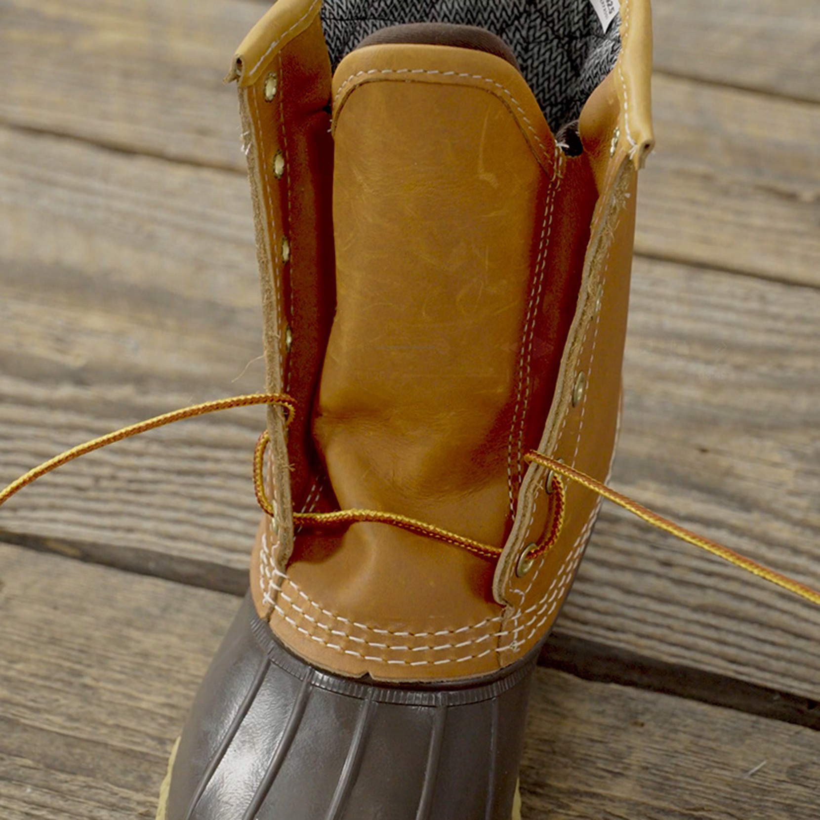 Close-up of an open brown leather boot with yellow laces on a wooden floor.
