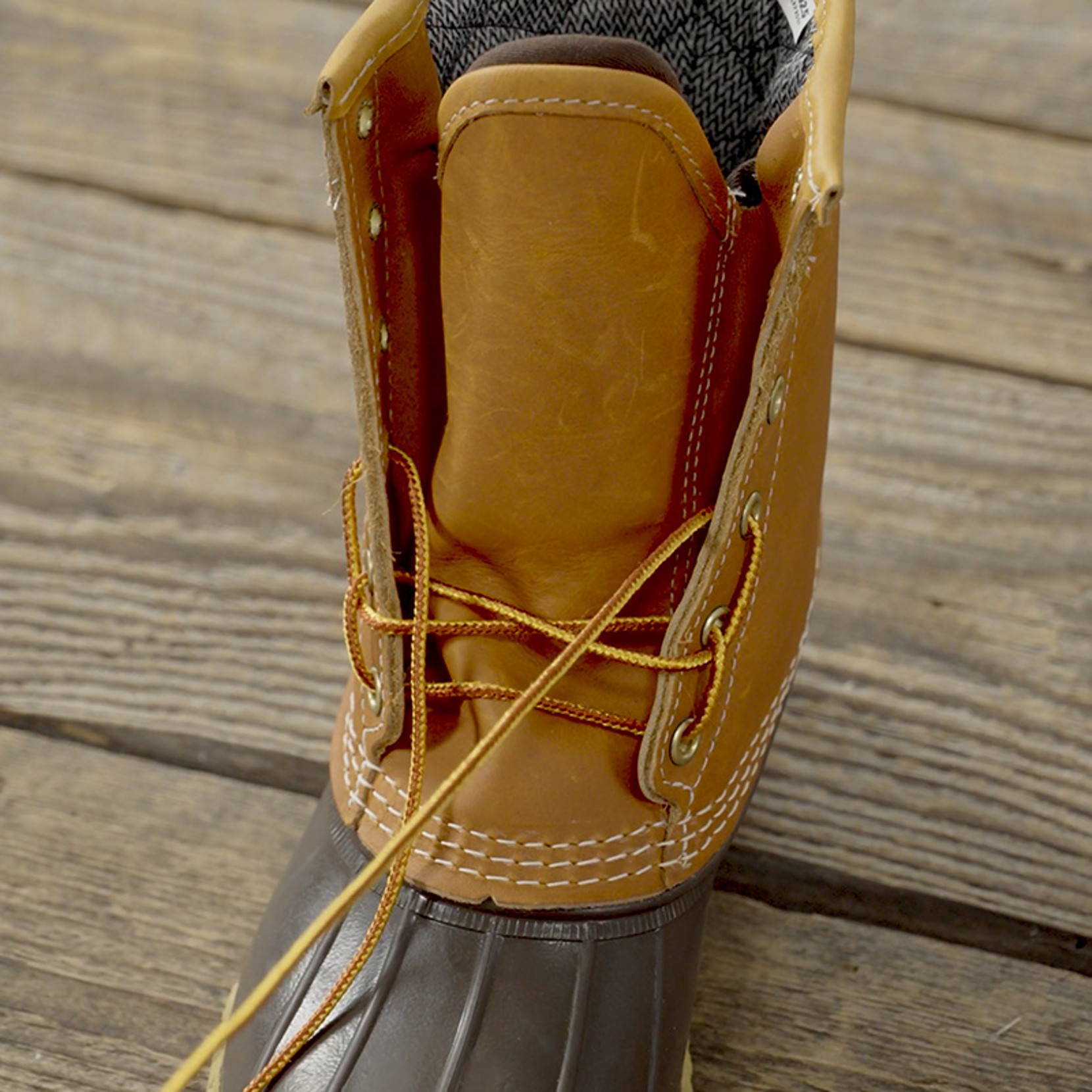 Close-up of tan and brown leather boot with yellow laces, partially unlaced, on a wooden surface.