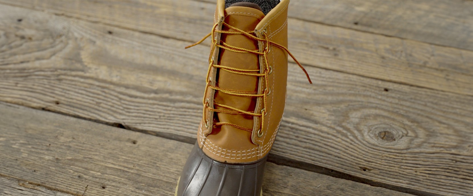 Close-up of a tan and brown boot with yellow laces on a wooden floor.