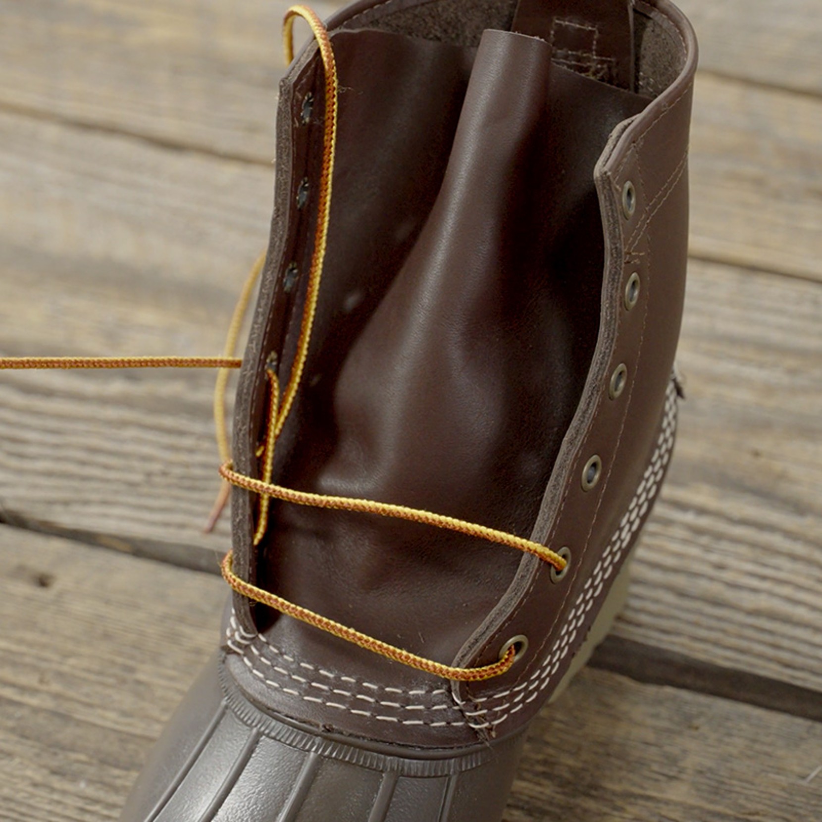 Brown boot with yellow laces partially threaded through metal eyelets.